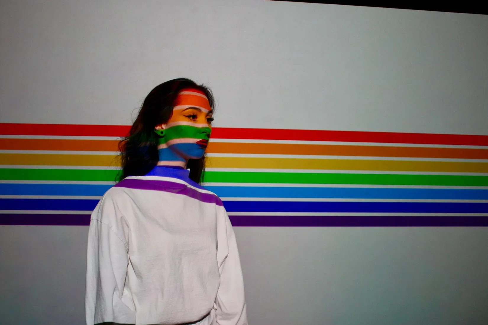 A girl stands against the background of a rainbow-painted wall